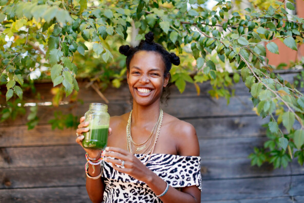 Black woman holding green juice while smiling.