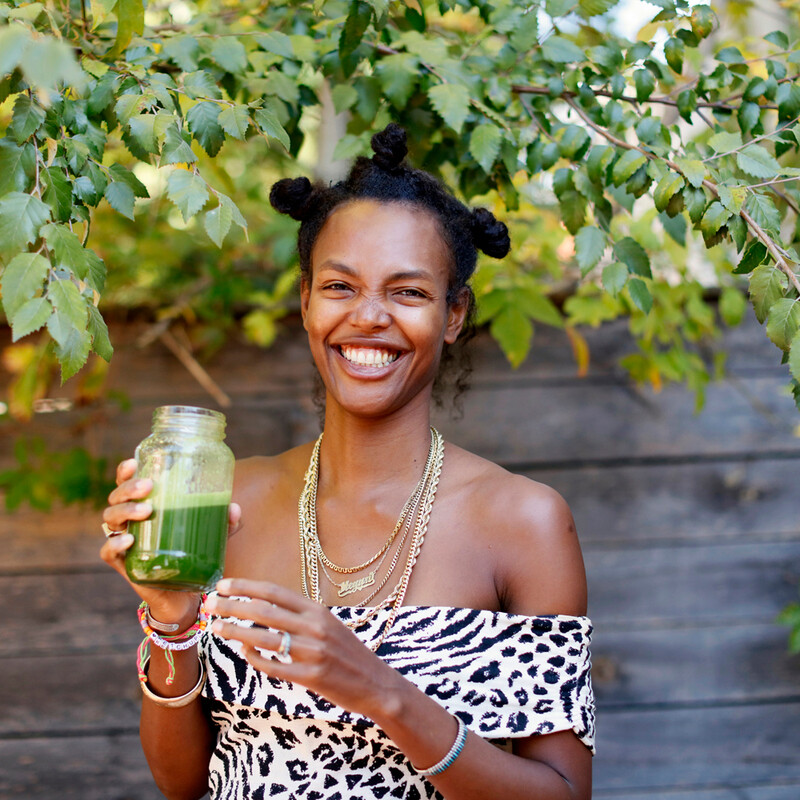 Black woman holding green juice while smiling.