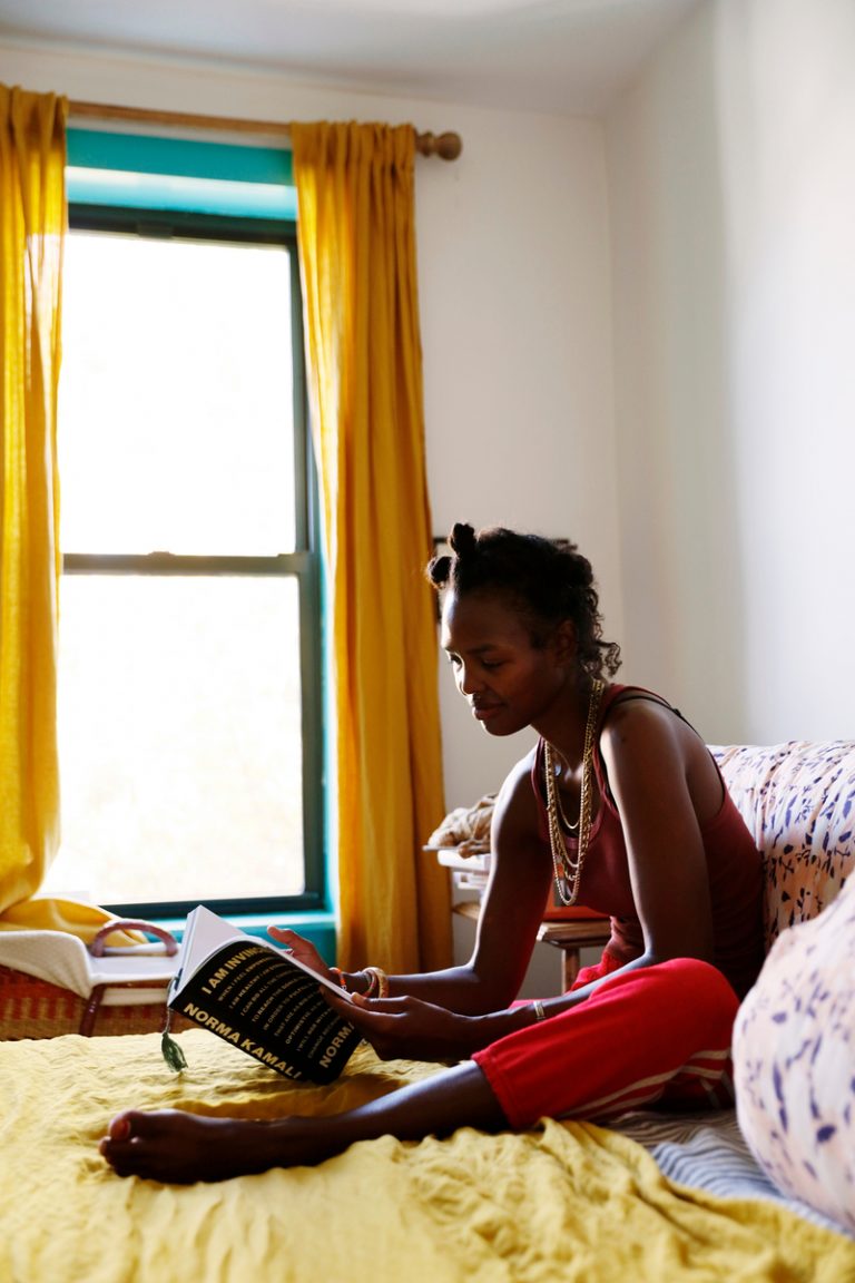 Black woman reading Norma Kamari's memoir in bed.