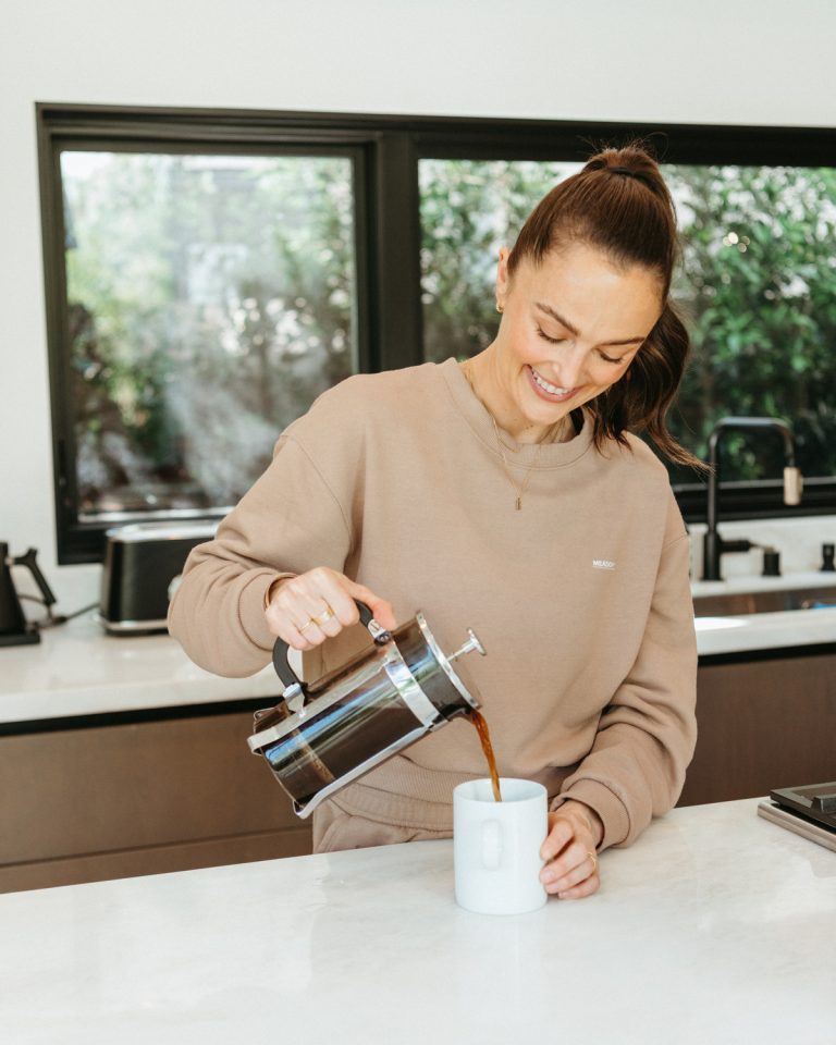 زن در حال ریختن قهوه کم اسید در لیوان سفید در آشپزخانه.
