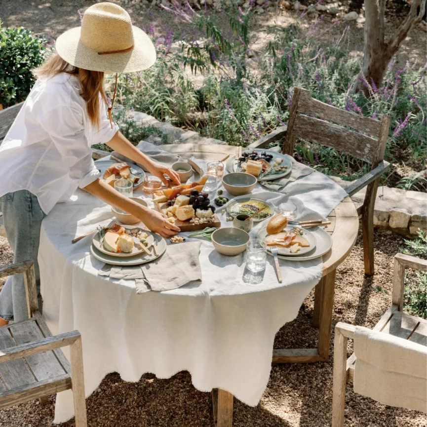 woman setting an outdoor dinner party table setting with linen throw