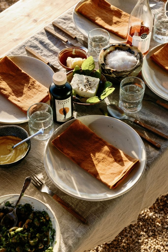 Outdoor table settings with natural linen tablecloth, speckled dining plates, and linen orange napkins.