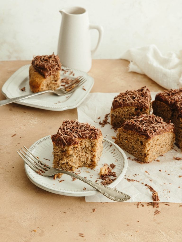 Squares of peanut butter banana snacking cake with chocolate frosting on two plates with forks.