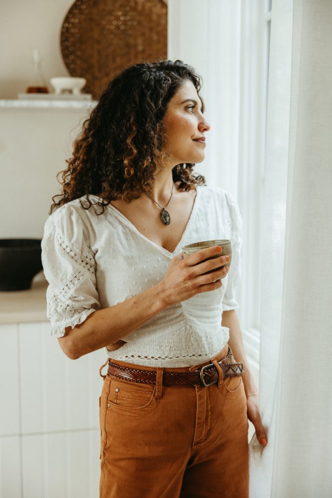 Brunette woman wearing white shirt holding mug of tea.