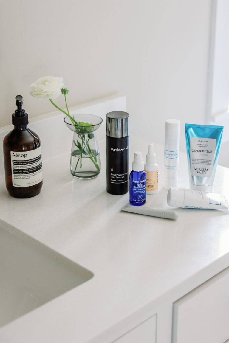 Various skincare products on white marble bathroom counter.