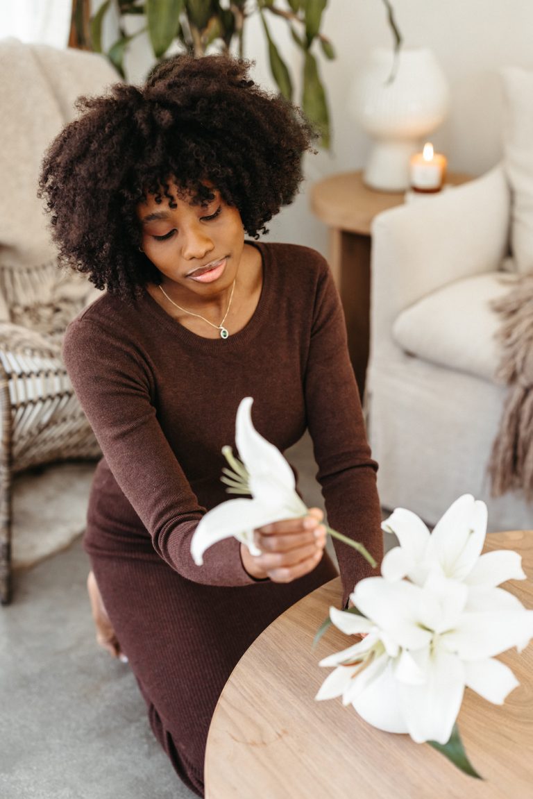 Black woman wearing brown sweater dress kneeling while arranging flowers.