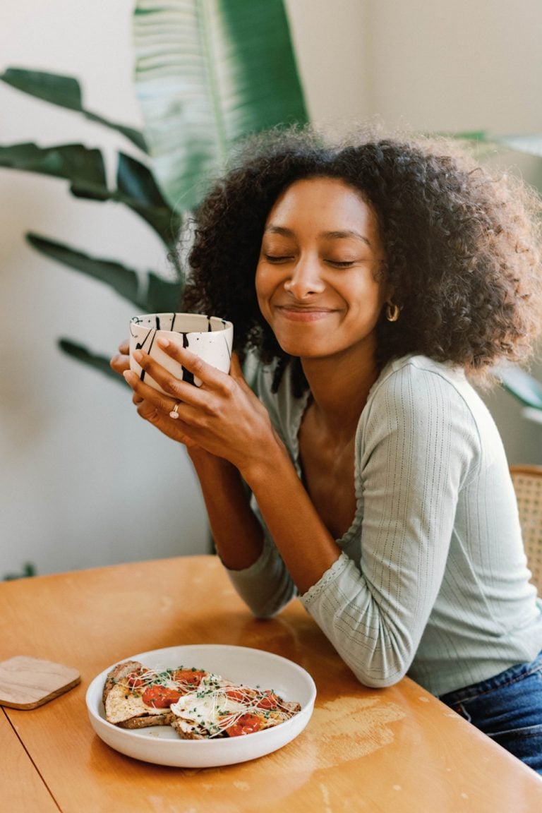 Black woman holding coffee mug smiling at breakfast table.