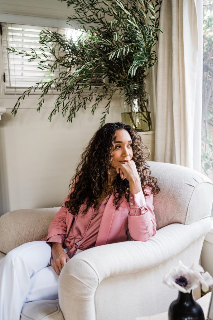 Simone Boyce wearing pink jacket sitting in cream-colored armchair.