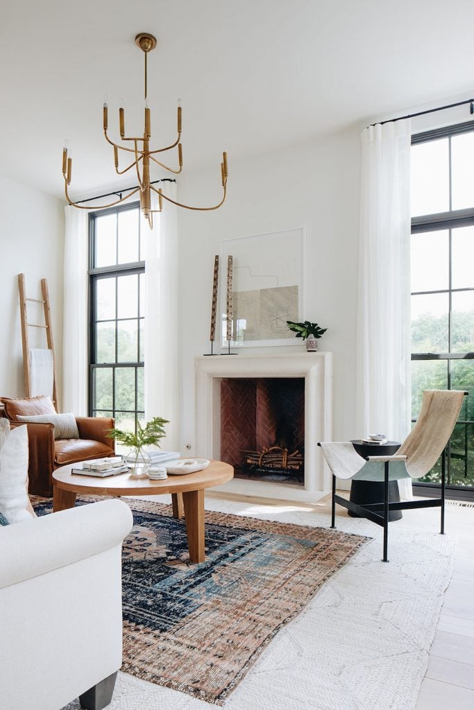 Quiet luxury trend in white modern living room with Moroccan rug, light wood coffee table, camel leather sitting chair, white couch, and large windows.