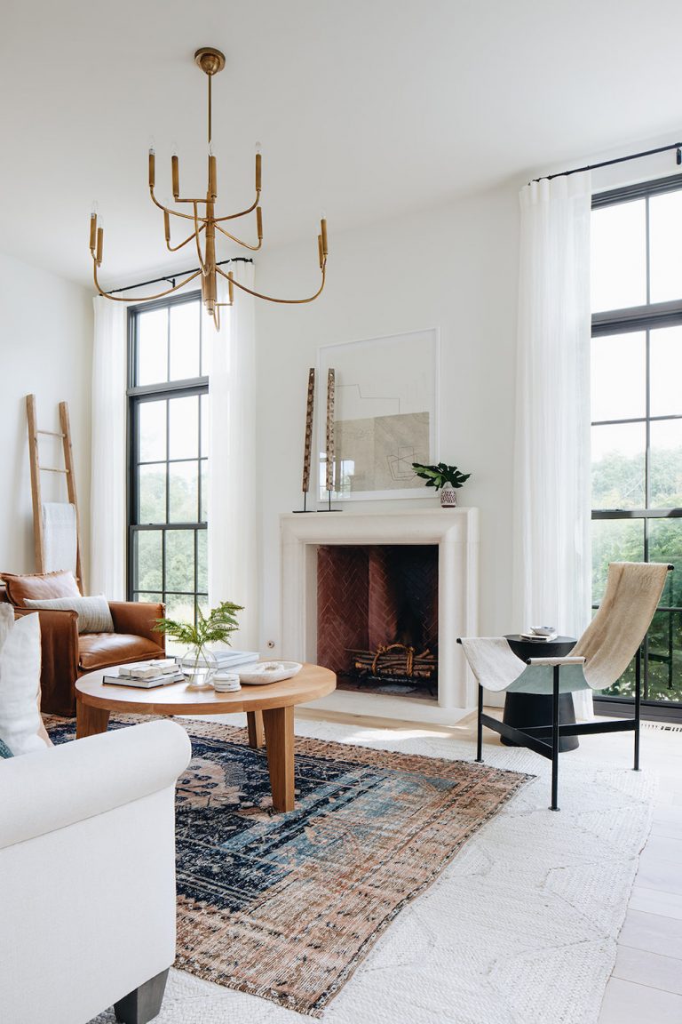 Quiet luxury trend in white modern living room with Moroccan rug, light wood coffee table, camel leather sitting chair, white couch, and large windows.