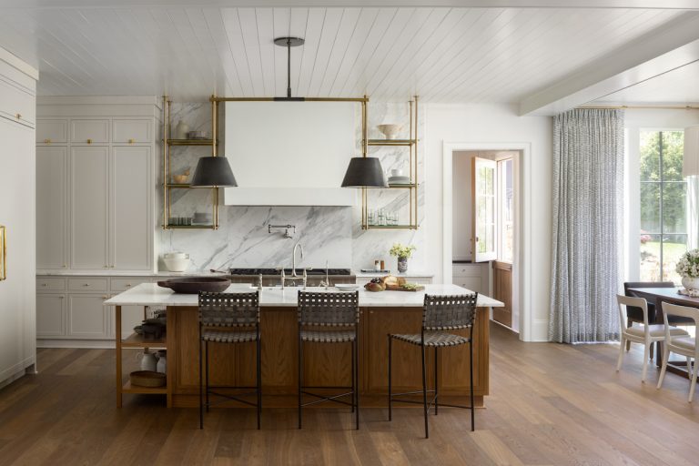 Modern white kitchen with hardwood floors, white cabinets, marble countertops, and countertop chairs at kitchen island.