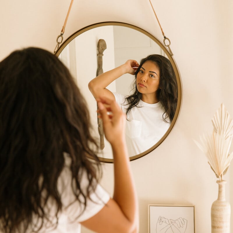 Brunette woman fixing hair in mirror.