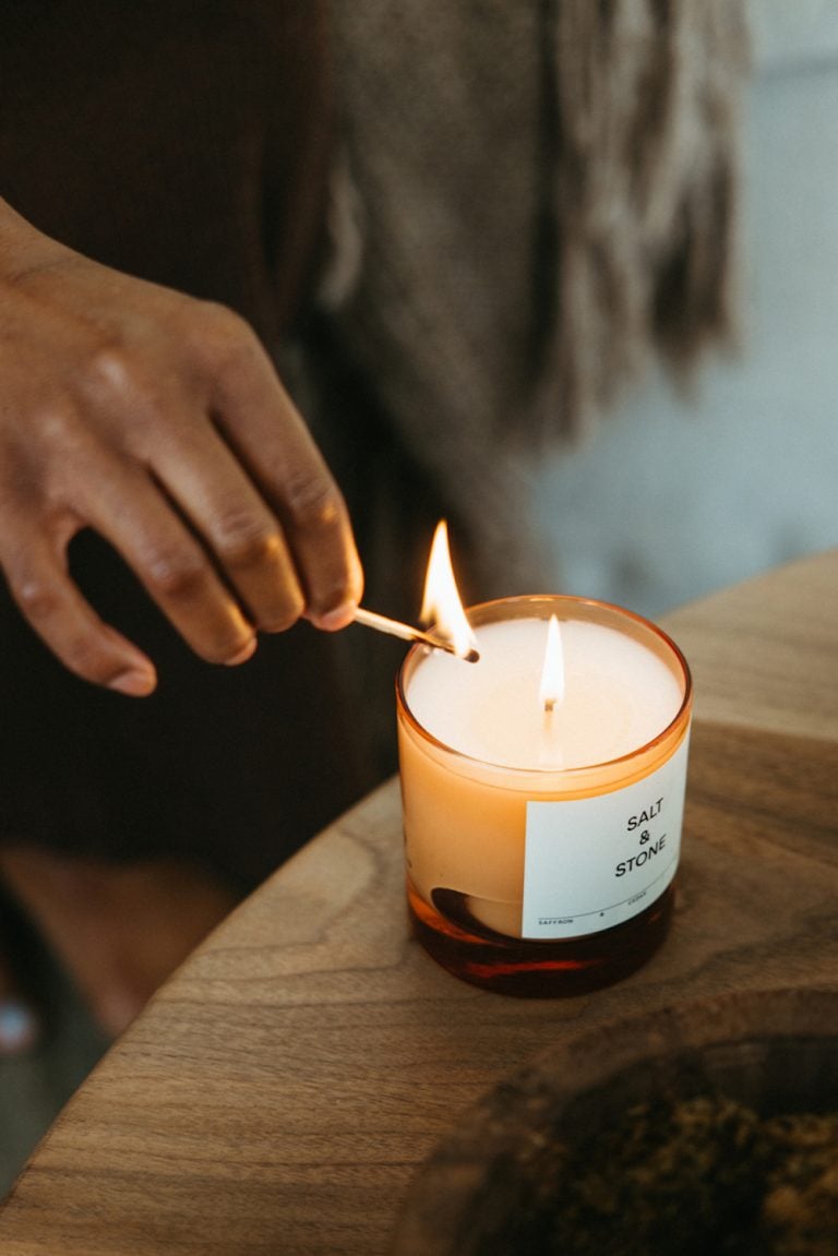 Black woman lighting Salt & Stone candle with match.