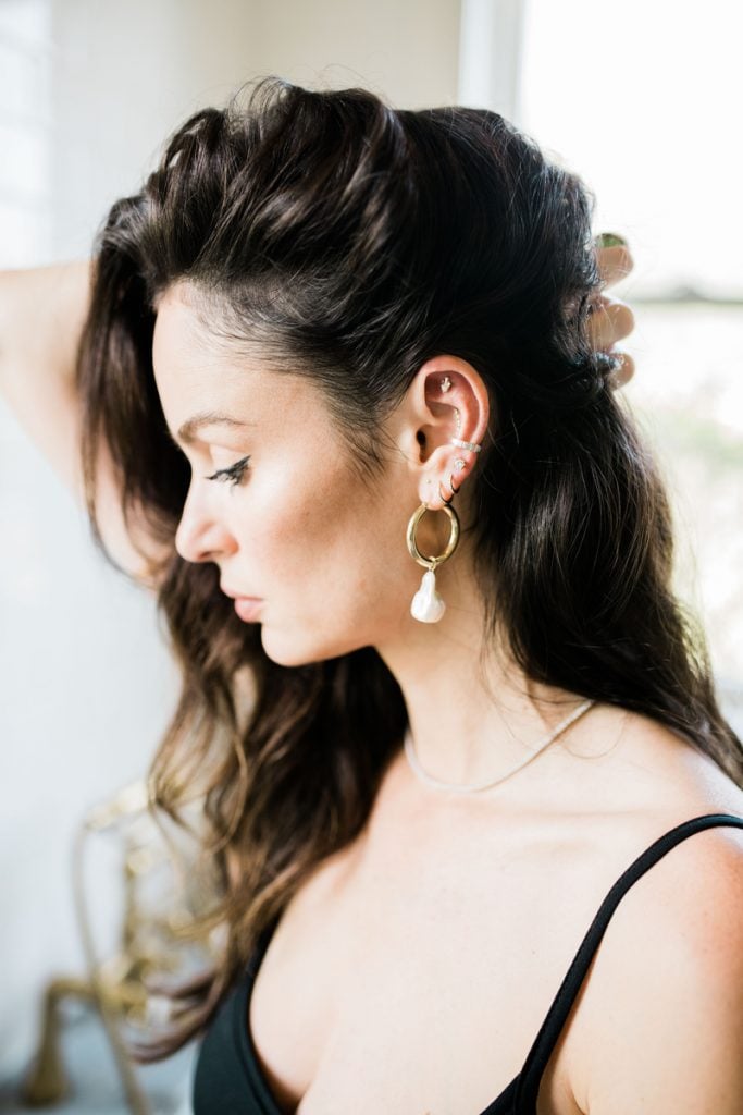 Brunette woman pulling back hair to show multiple ear seeds.