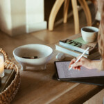 Woman journaling at coffee table on iPad.