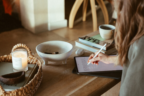 Woman journaling at coffee table on iPad.