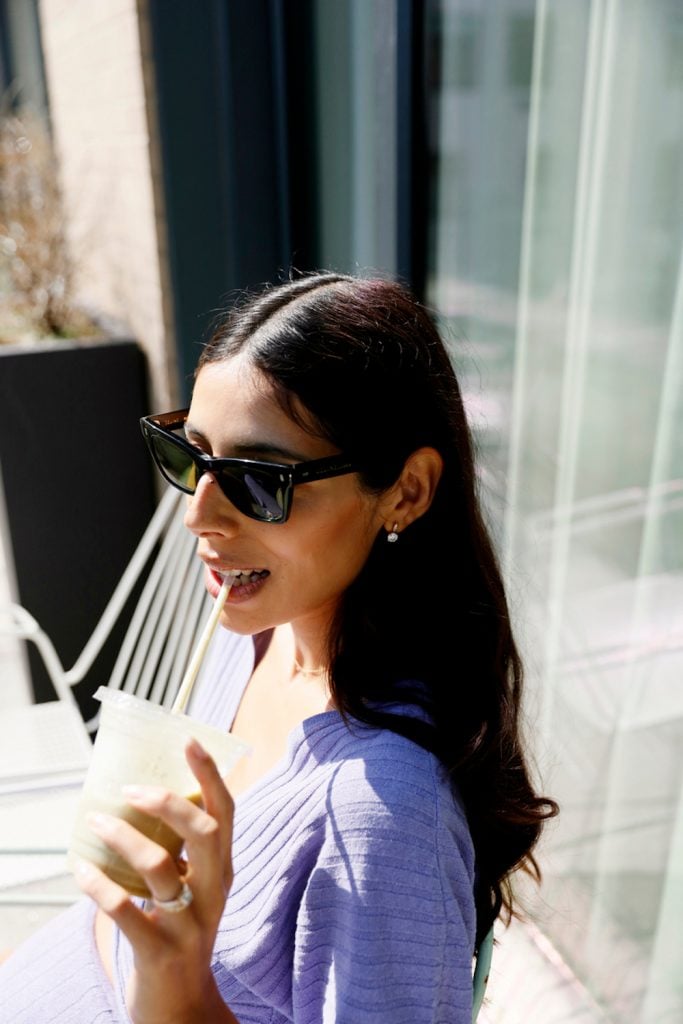 Brunette woman wearing sunglasses drinking iced coffee from straw outside.