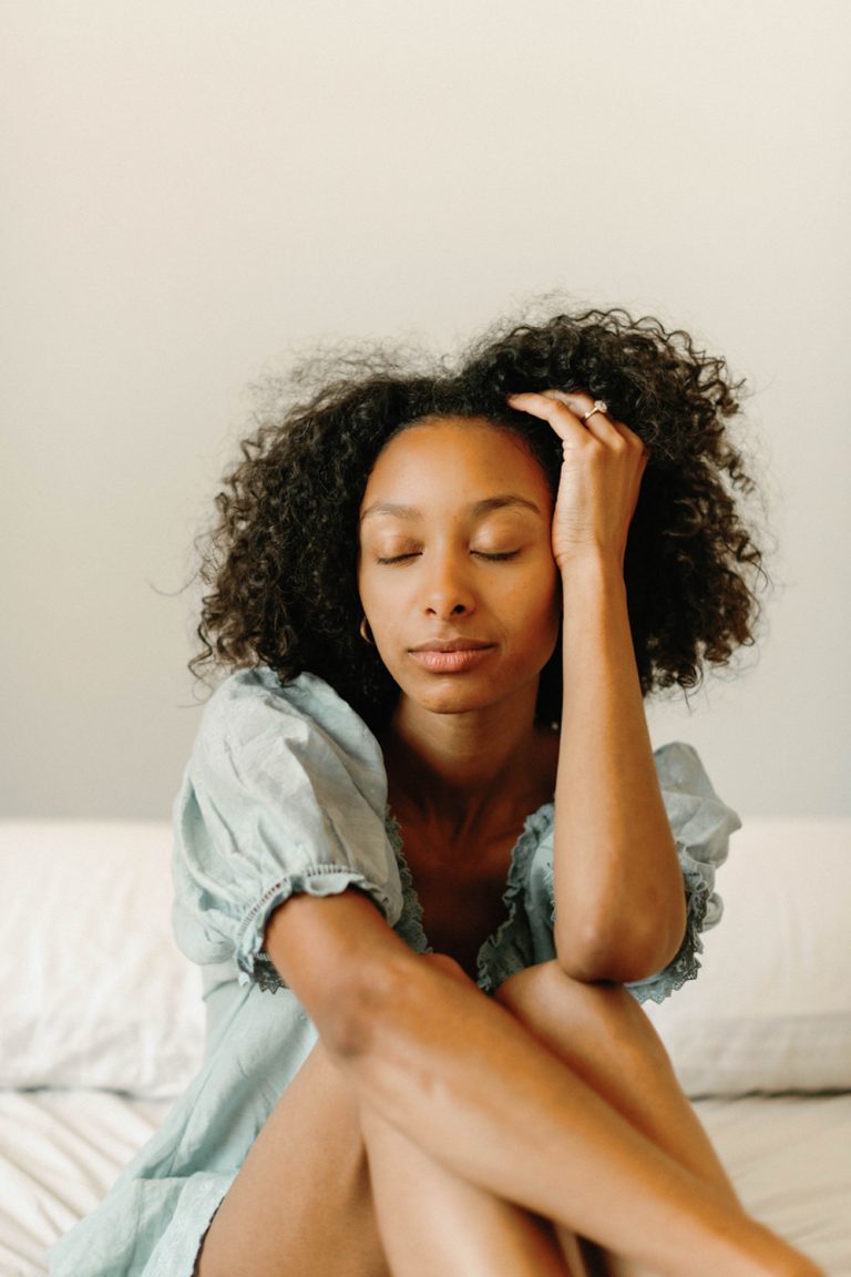 Woman wearing nightgown sitting on bed with closed eyes.