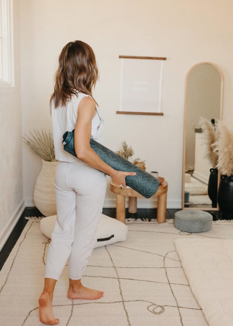 Woman carrying yoga mat in meditation room.