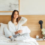 Camille Styles wearing loungewear drinking glass of water in bed.