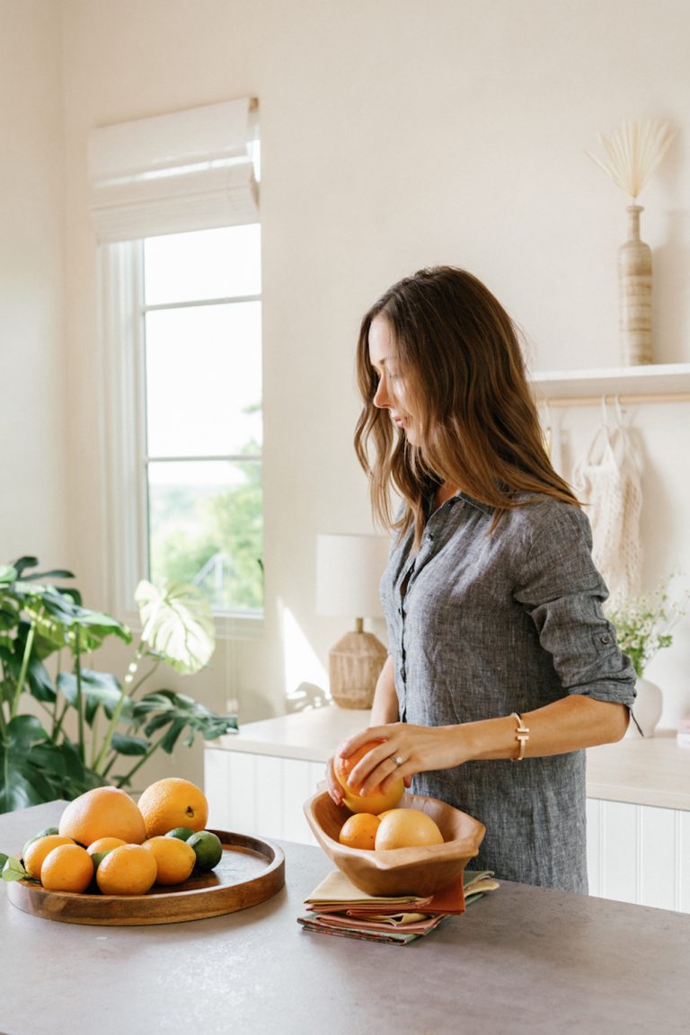 Brunette woman peeling citrus fruits at kitchen counter.