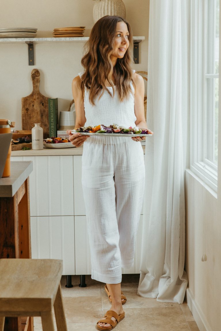 Camille Stiles in a white linen shirt and pants carrying a platter of food.