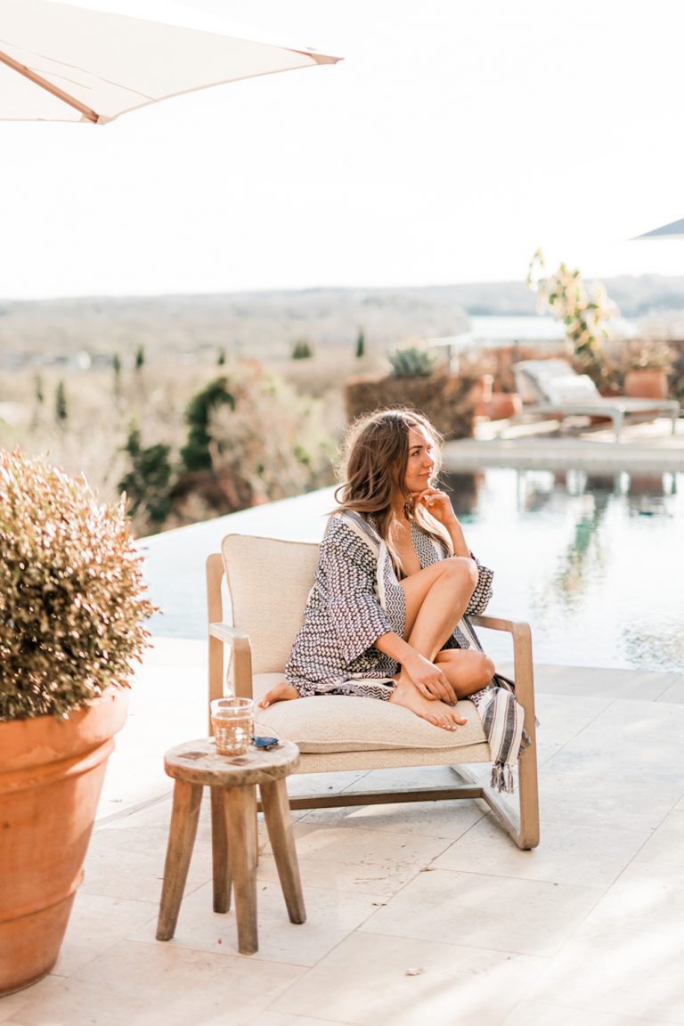 Brunette woman wearing summer loungewear sitting on chair next to pool.