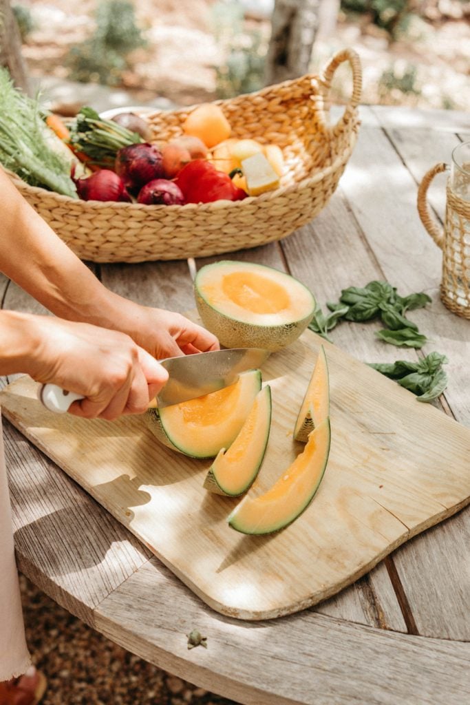 Slicing up cantaloupe on wooden cutting board.