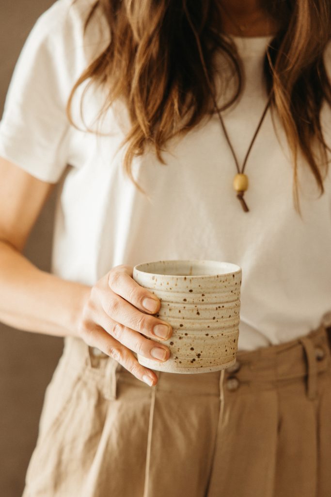 Woman holding white speckled ceramic coffee mug.