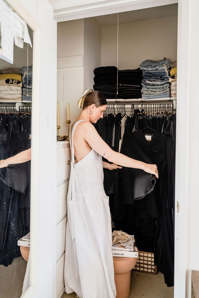 Brunette woman organizing clothes in closet.