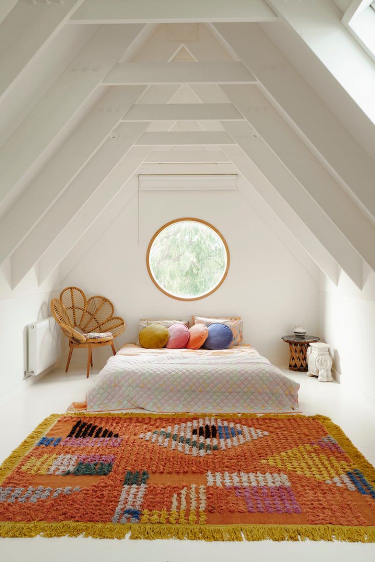 Boho bedroom with white walls and bright rug.