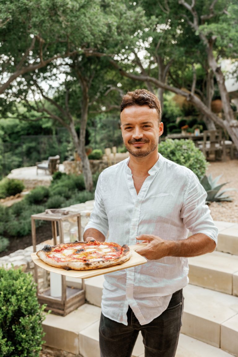 Un hombre con una camisa blanca sostiene una pizza afuera.