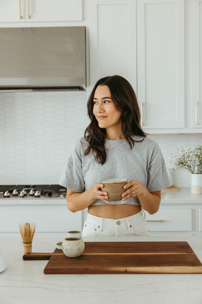 Brunette woman sipping matcha in all-white kitchen.