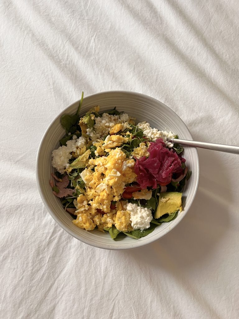 Scrambled eggs, cheese, greens, and beet sauerkraut in white bowl.