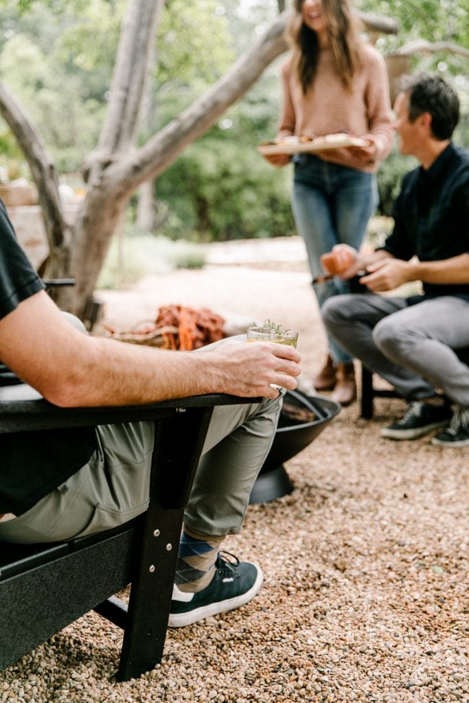 Men sit around an outdoor fire pit in Adirondack chairs.