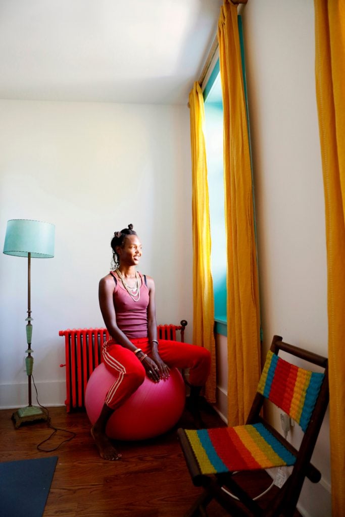 Black woman sitting on pink exercise ball looking out window.