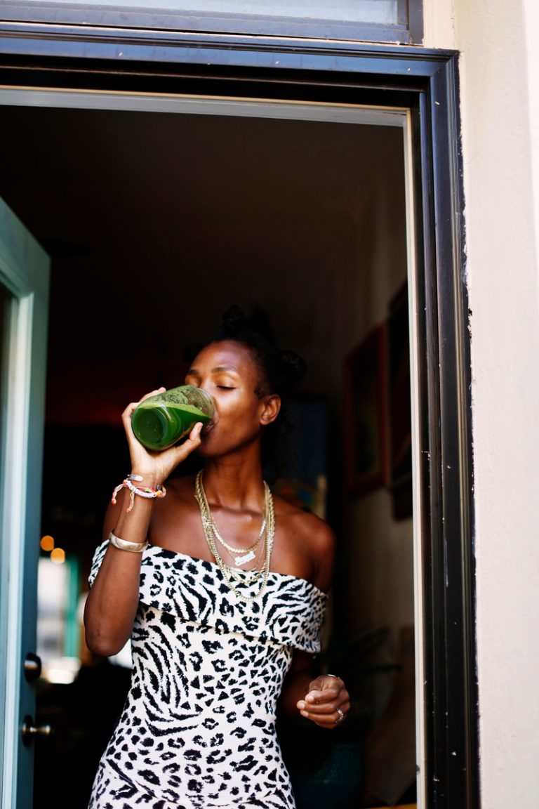 Black woman drinking green juice wearing zebra-print dress.