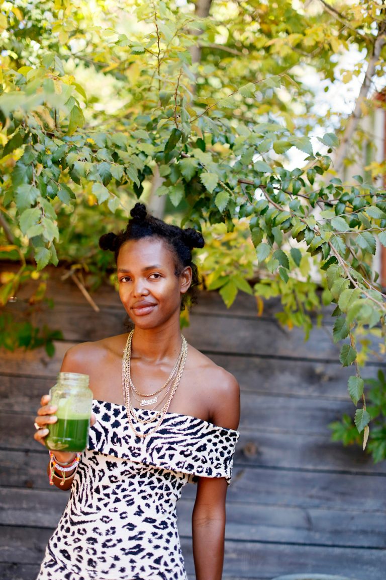 Black woman wearing zebra-print dress drinking green juice.