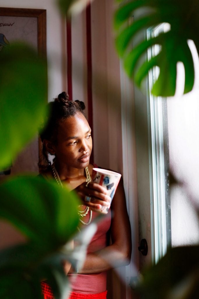 Black woman holding mug looking out window.