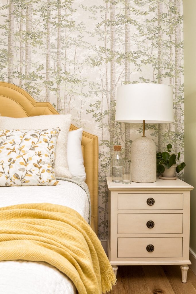 Cottage-style bedroom with neutral nightstand, table lamp, and wallpaper accent wall.