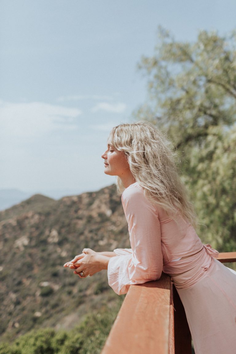 Blonde woman wearing pink drink deep-breathing outside.