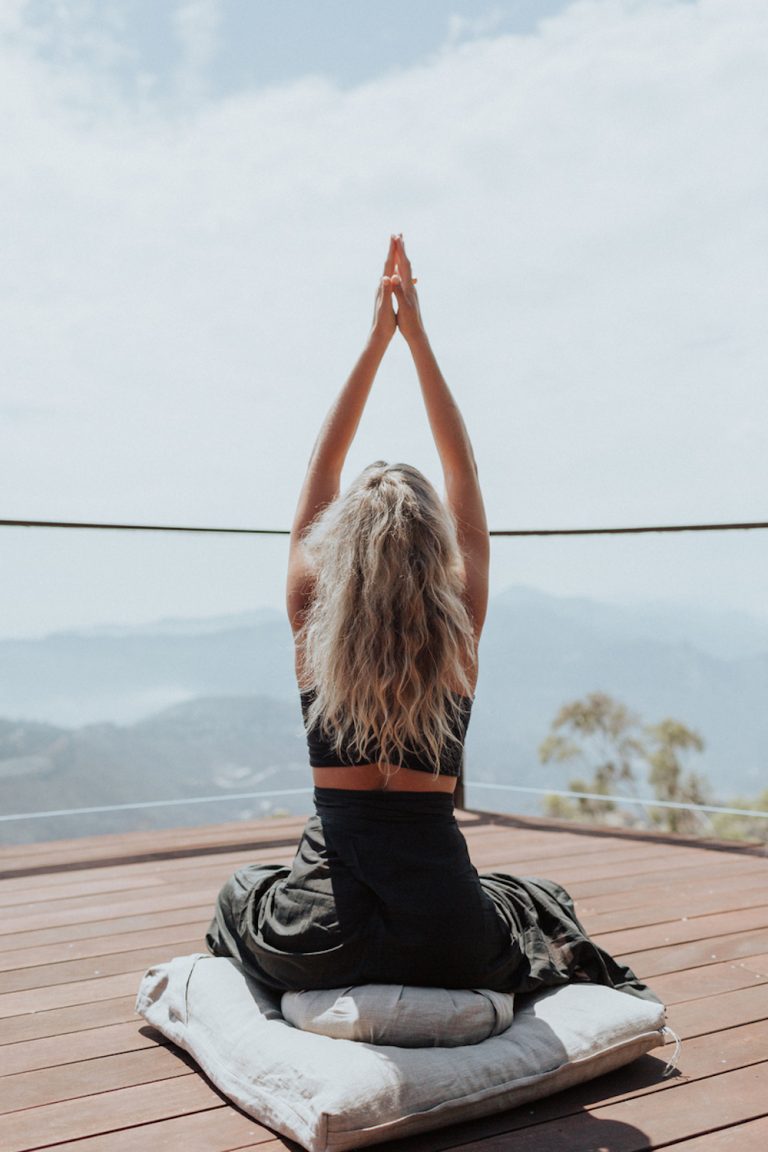 Blonde woman doing yoga on deck outside.