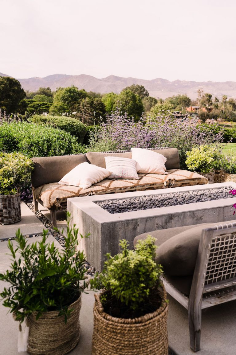 Rectangular concrete outdoor fire pit surrounded by outdoor couches and greenery.