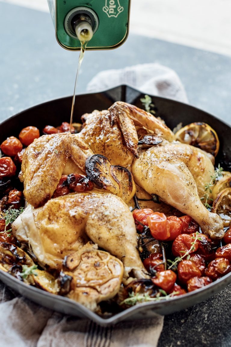 pouring olive oil on roasted chicken with cherry tomatoes