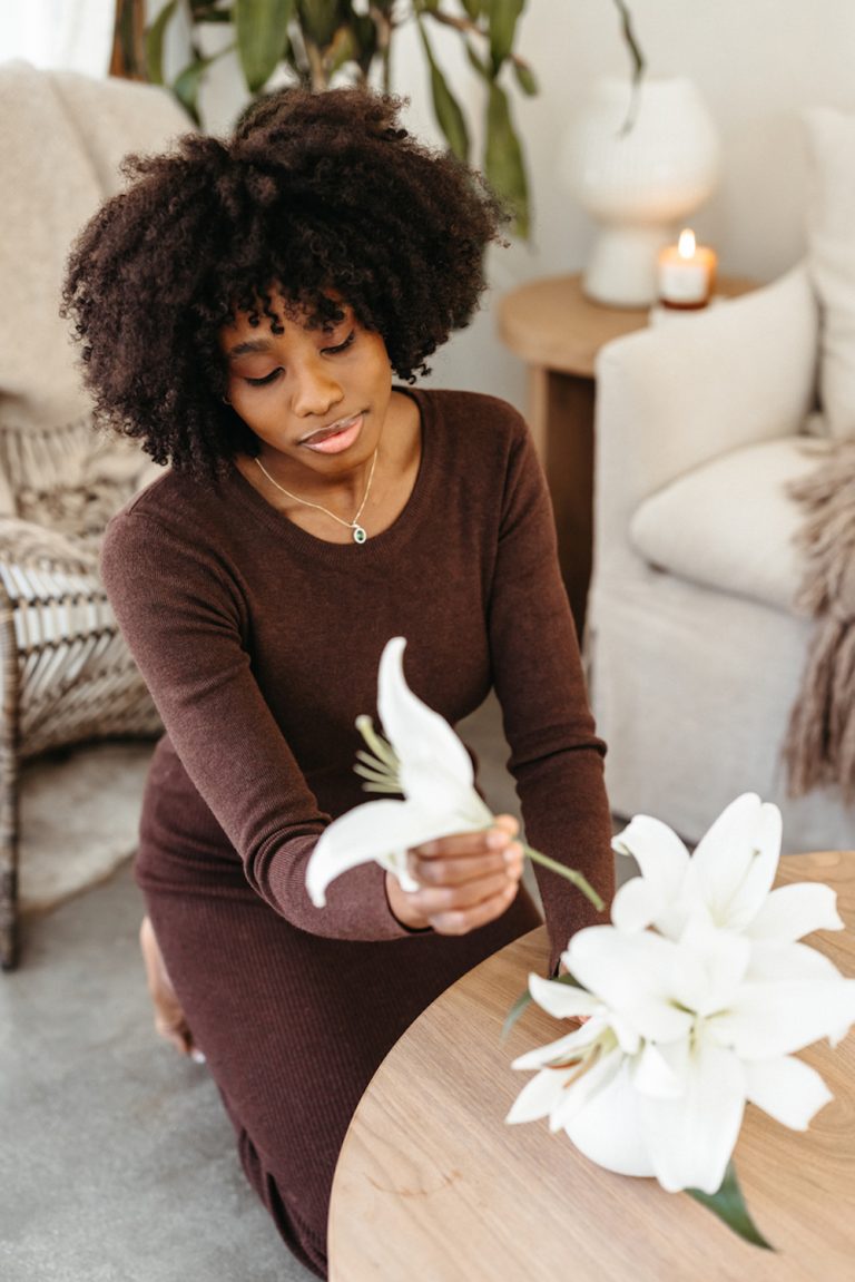 Black woman with short afro hair arranging white flowers in a vase.