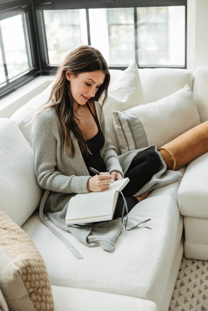 Woman writing in journal on couch.