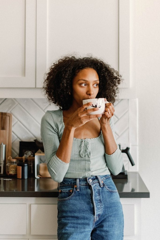 Woman drinking cup of coffee in kitchen.