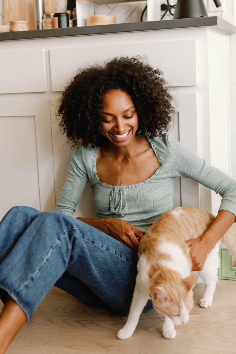 Woman sitting on kitchen floor playing with orange cat.