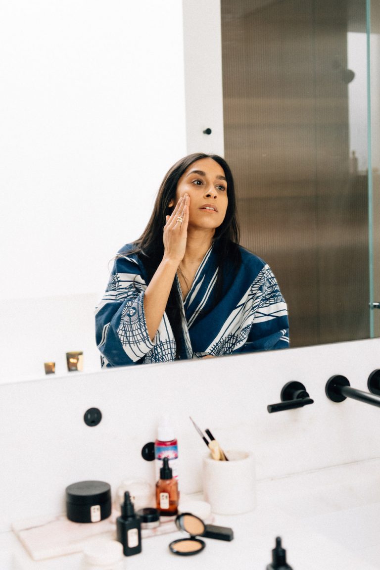 Brunette woman applying skincare in bathroom mirror.