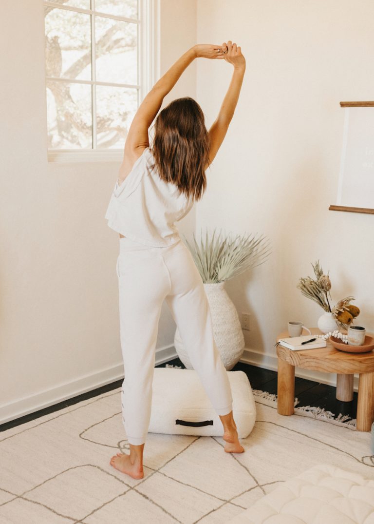 Brunette woman in white pants and shirt stretching in yoga studio.